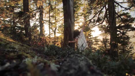 A-young-adult-woman-in-a-white-dress-leans-on-a-tree-while-enjoying-the-beautiful-sunlight-of-golden-hour-and-sunbathing