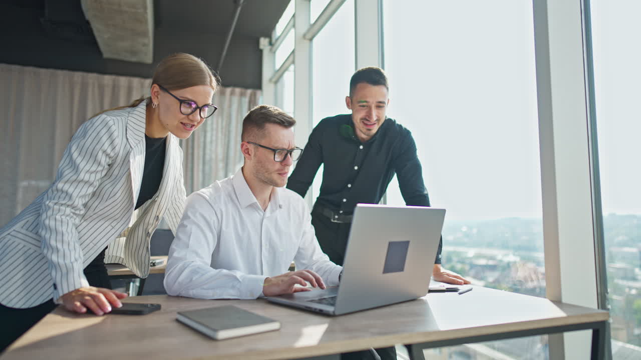Office employees cooperation at work. Three colleagues looking at laptop discussing job issues. Panoramic windows at backdrop.