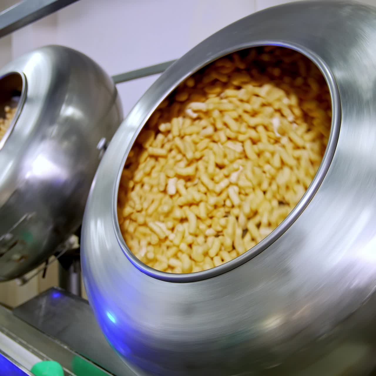 Two metal tanks full of sweet snacks rotating and mixing. Tasty snack product manufacturing at modern plant