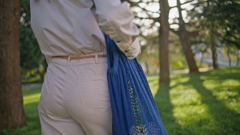 conscious woman carrying eco reusable shopping bag in green sunny park closeup.