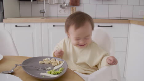 cute baby girl sitting in high chair next to the kitchen table eating food with hands