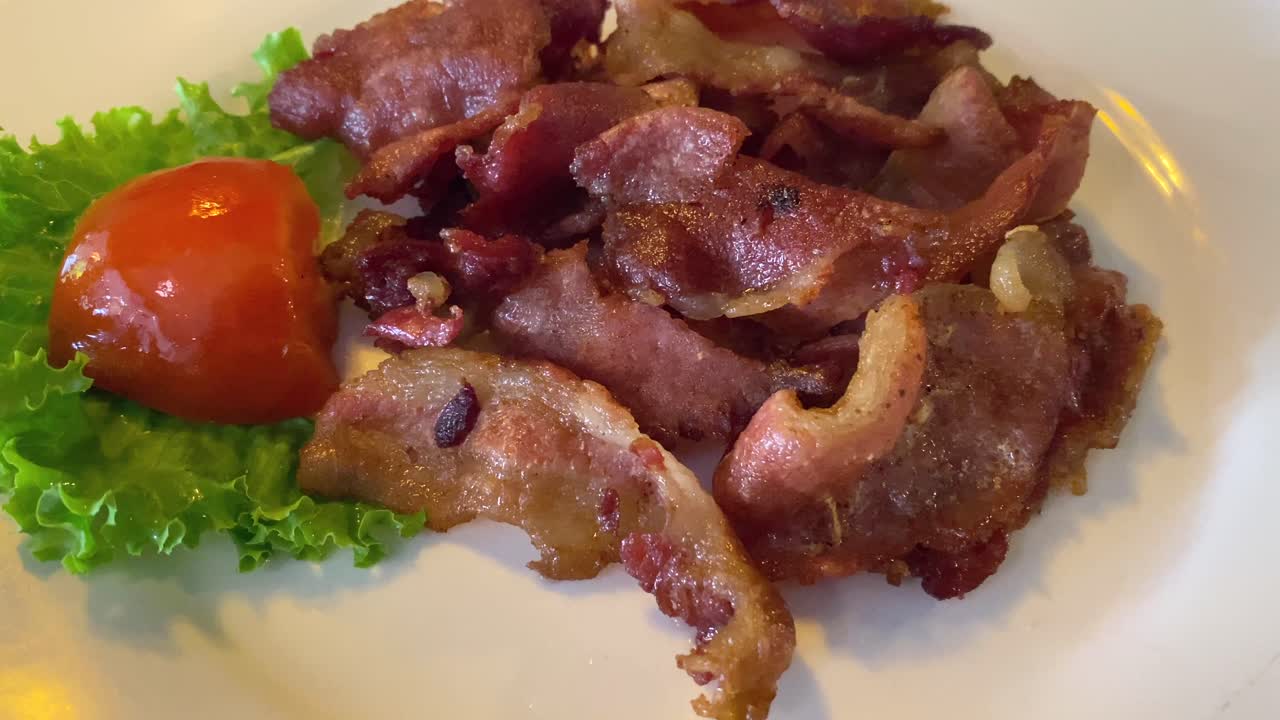 A plate of fried bacon with a tomato and a piece of lettuce
