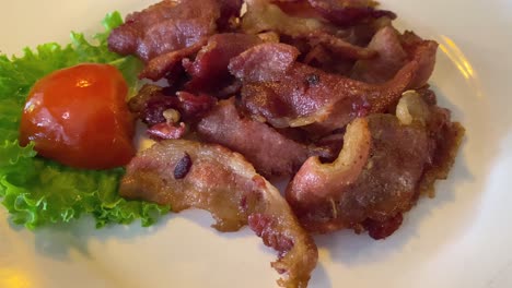 a plate of fried bacon with a tomato and a piece of lettuce