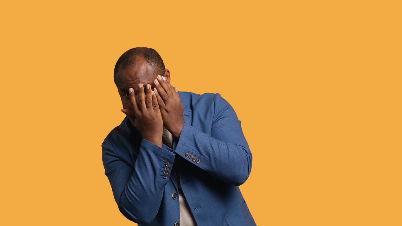 Man covering face with hands to avoid being recognized, studio background