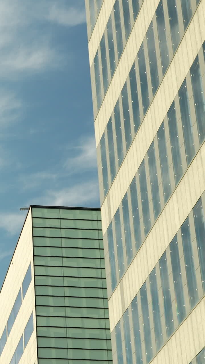 Uno scatto verticale di facciate di edifici per uffici contemporanei con pannelli di vetro e motivi geometrici contro un cielo blu. Ideale per contenuti di business e sviluppo urbano