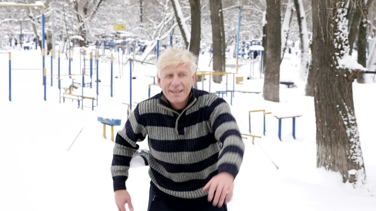 un anciano europeo hace un calentamiento al aire libre por la mañana en invierno, ejercicio para un calentamiento de la espalda, se inclina hacia adelante. concepto de vida saludable. 60 fps