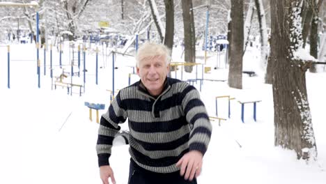 an elderly european man does a morning outdoor warm-up in the winter, exercise for a warm-up of the back, leanings forward. healthy life concept. 60 fps