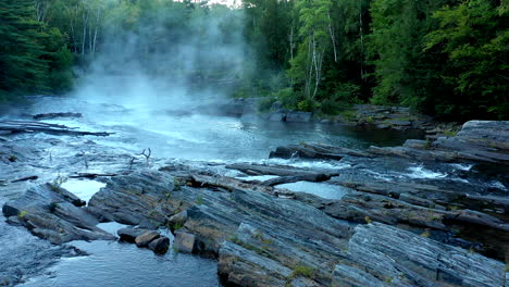 disparo aéreo de drones volando bajo sobre las oscuras rocas húmedas y el arroyo del bosque brumoso en big wilson falls durante el atardecer en maine