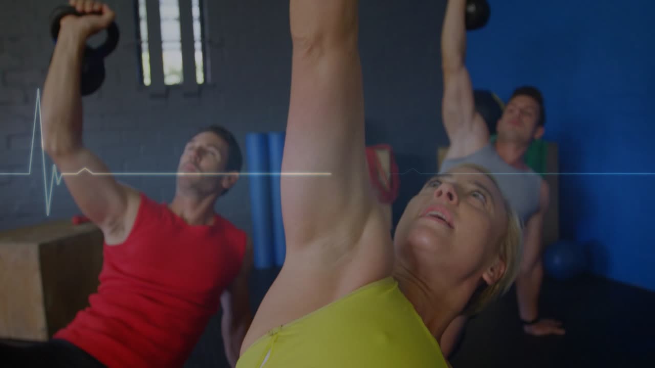 Woman and group pressing kettlebells on cue ECG peaking with arms reaching overhead for fitness