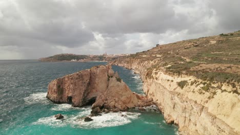 Aerial-reverse-flying-drone-shot-capturing-Gozo's-rugged-coast,-the-drone-reveals-the-intricate-details-of-the-rocky-formations-below,-juxtaposed-against-the-lively-turquoise-sea