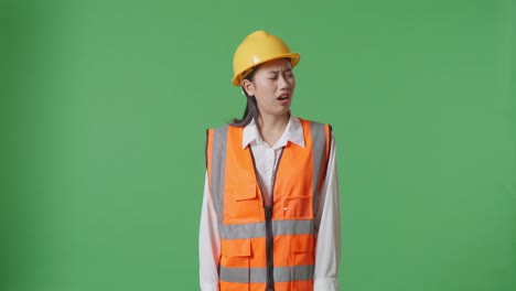 wondering asian female engineer with safety helmet working doubtfully in the green screen background studio