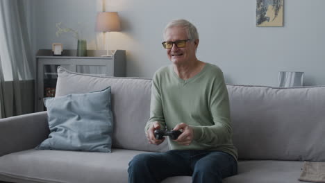 Glücklicher-älterer-Mann,-Der-Videospiel-Spielt,-Während-Er-Zu-Hause-Auf-Dem-Sofa-Sitzt-1
