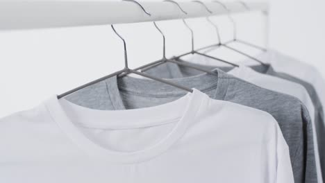 video of white and grey t shirts on hangers and copy space on white background