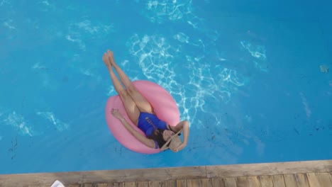 mujer feliz relajándose en la piscina en un anillo rosa inflable