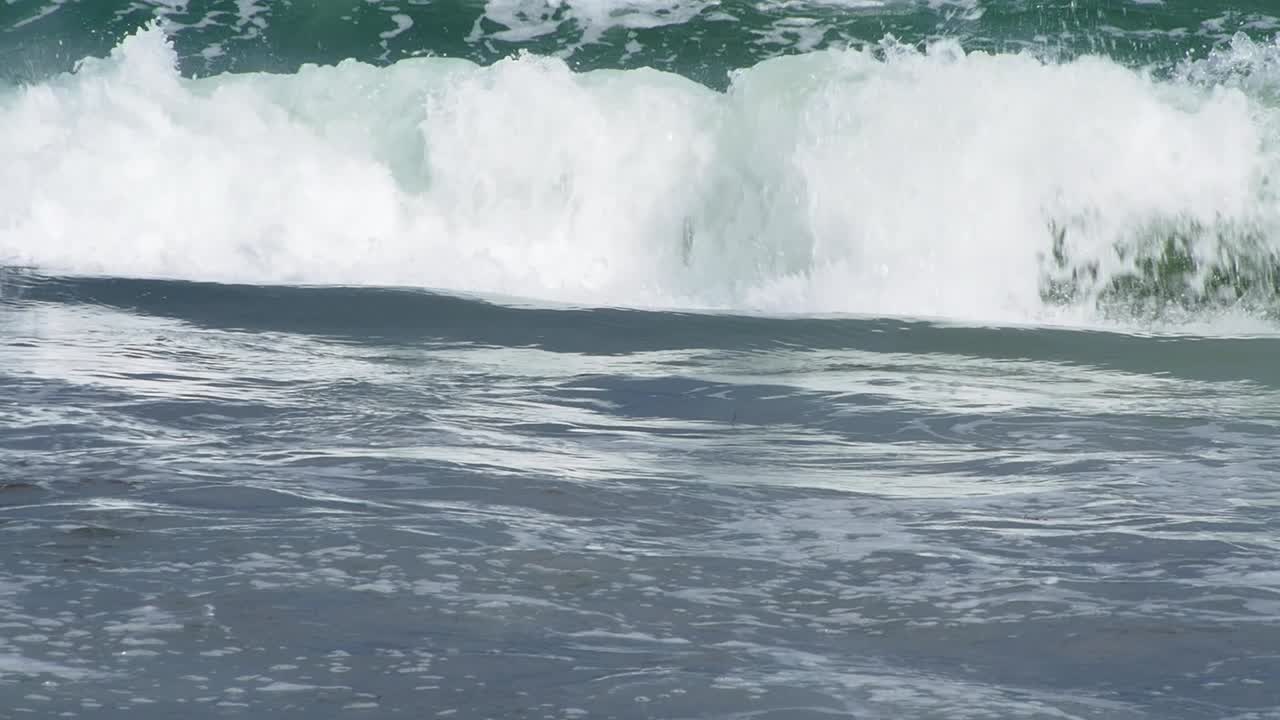 작은 파도가 거품 스와시로 부서지고 해안으로 굴러갑니다.