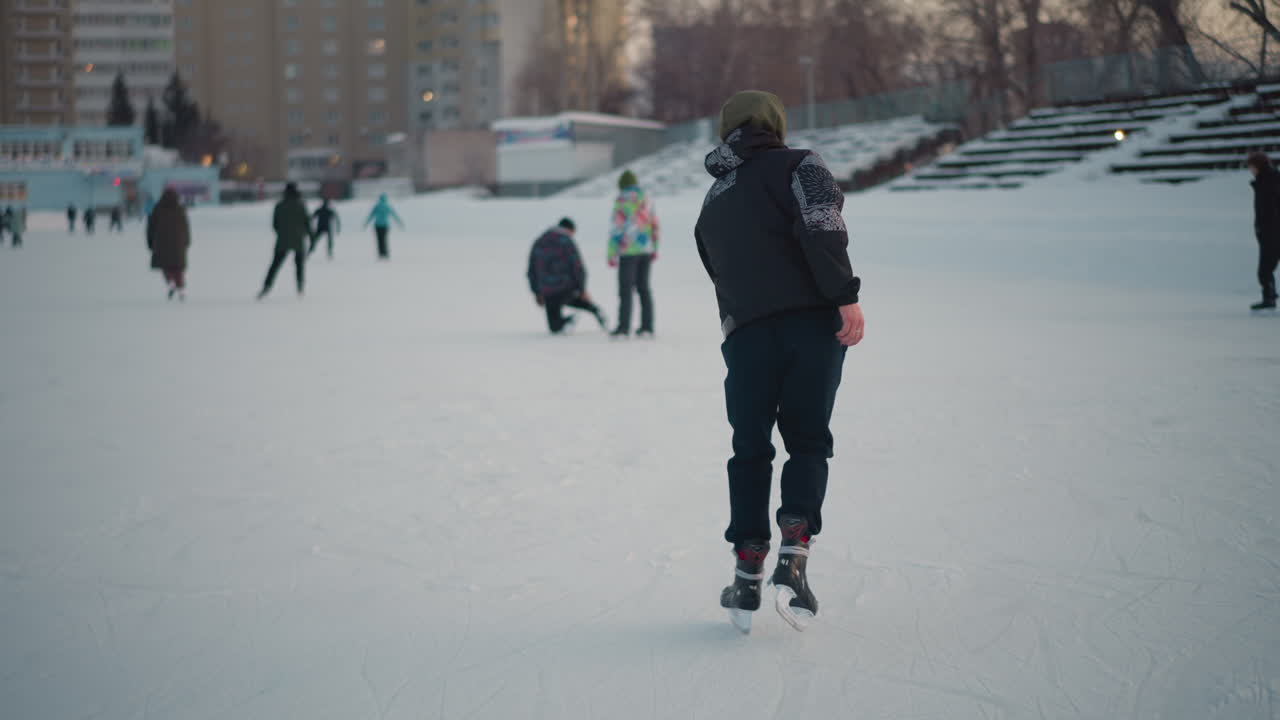 expert skater showcasing advanced moves on snowy urban ice rink, smooth gliding and confident posture against backdrop of fellow skaters and residential buildings under soft winter light