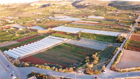 farmland plots of plowed land and industrial greenhouses in malta, aerial side fly view