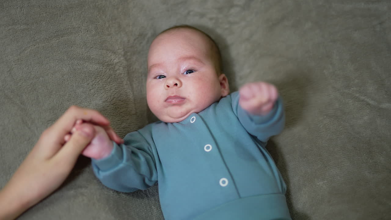 Mommy is taking baby's little hand into hers. Adorable infant boy waving his fists and looking into camera. Close up.