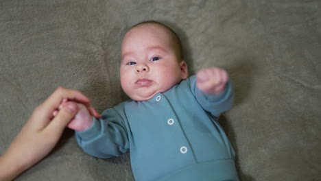 mommy is taking baby's little hand into hers. adorable infant boy waving his fists and looking into camera. close up.