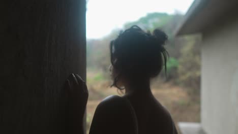 silhouetted young woman gazing out a window in a dimly lit room, evoking a sense of contemplation and solitude