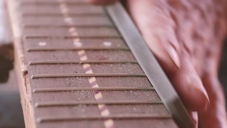 luthier files frets on neck of classical guitar in madeira, portugal