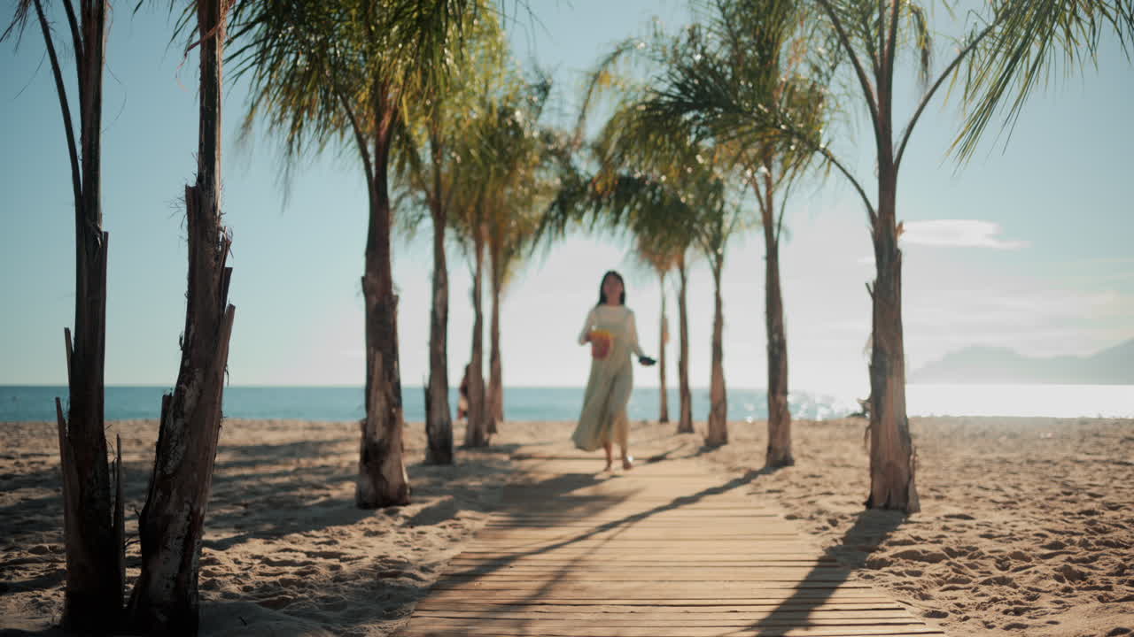 Wooden walkway surrounded by palm trees leading to a sunny beach with clear blue water