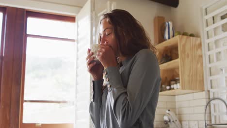 happy caucasian woman standing in sunny cottage kitchen enjoying drinking coffee and smiling