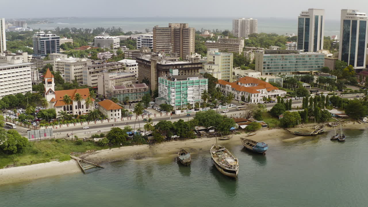 la vista de la costa de la ciudad de dar es salaam, tanzania, con edificios administrativos, iglesia católica, playa y barcos en la costa.