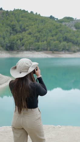 woman photographing a scenic turquoise lake and mountains