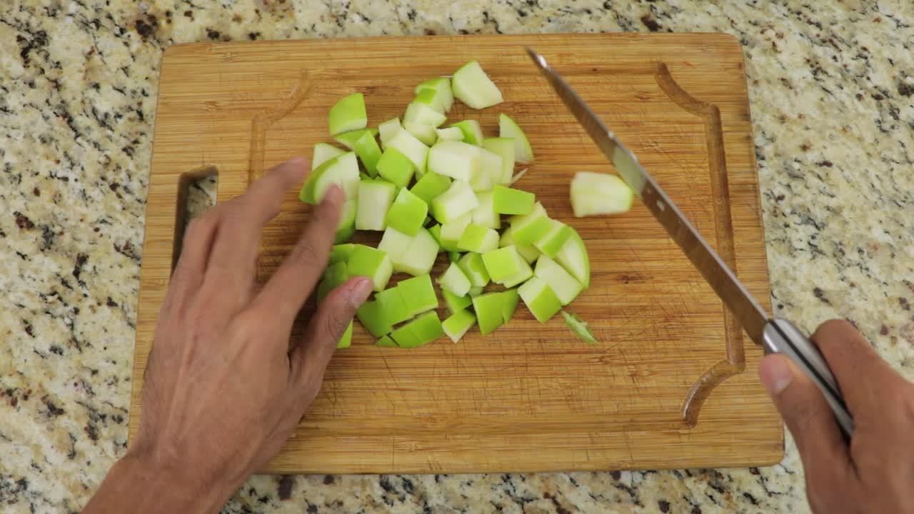 POV cutting green apple into cubes with knife on cutting board