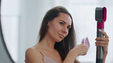 Charming-girl-styling-hair-at-mirror-place-close-up.-Woman-brushing-chevelure