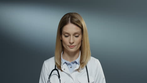 Primer-Plano-De-La-Guapa-Mujer-Feliz-Médico-Sonriendo-Y-Mirando-A-La-Cámara-En-El-Fondo-Gris