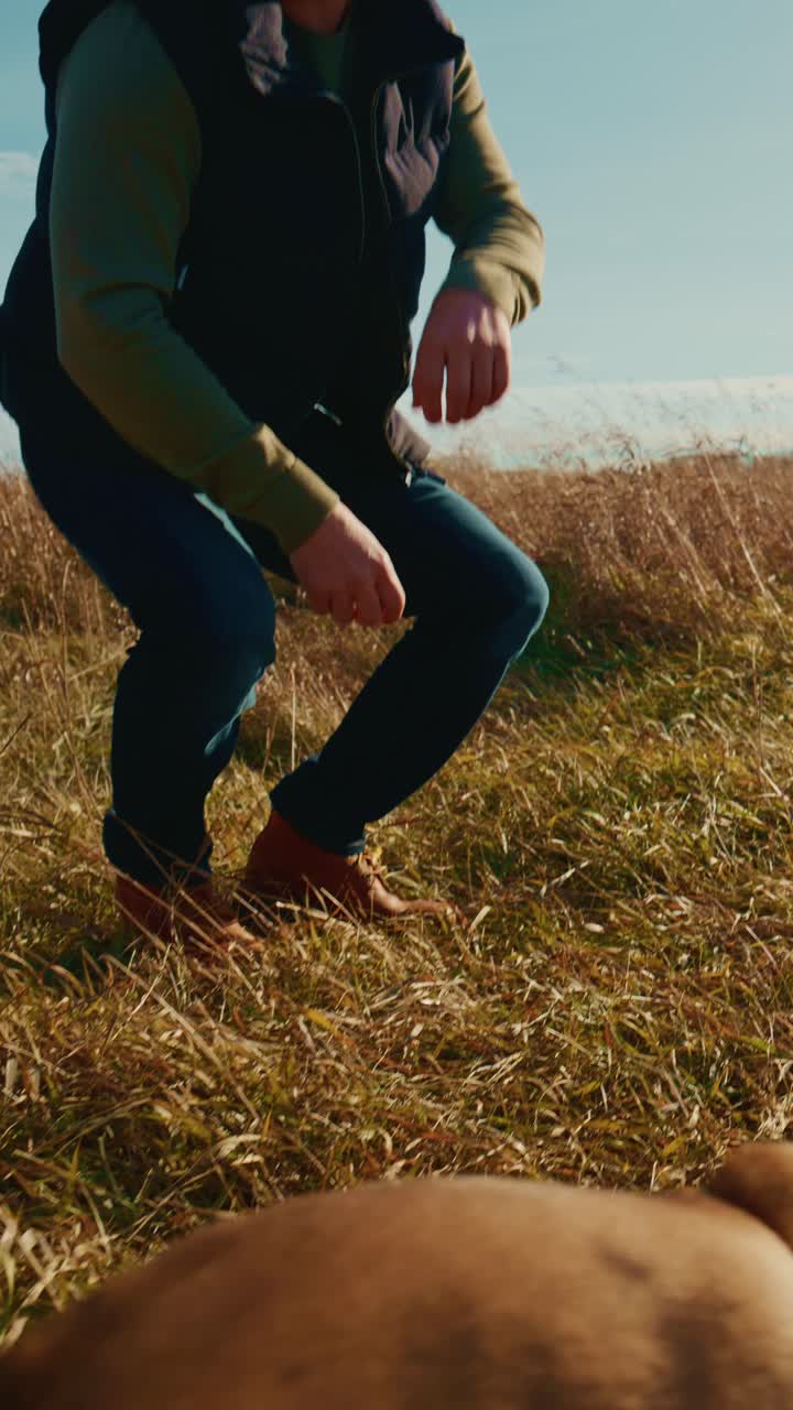 A Joyful Interaction Between a Man and His Playful Dog in a Scenic Open Field, Highlighting Their Bond Through Playtime with a Colorful Toy Under a Clear Blue Sky