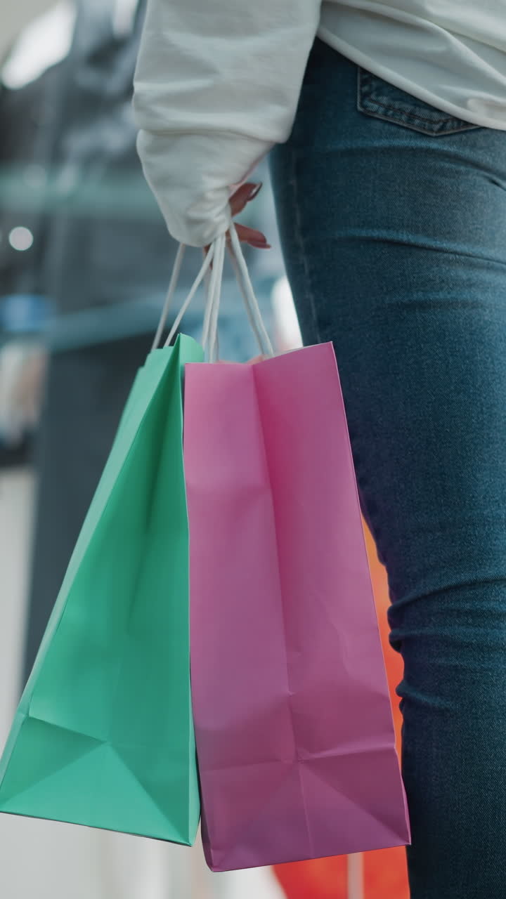vista trasera de una mujer de pie con bolsas de compras balanceándose suavemente en un centro comercial bien iluminado, el fondo muestra exhibiciones de ropa en tiendas con colores vibrantes y entorno minorista moderno