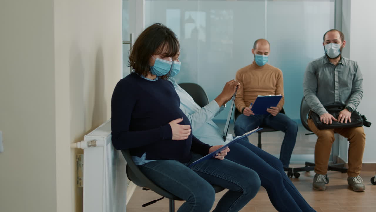 Pregnant woman with face mask sitting in waiting queue