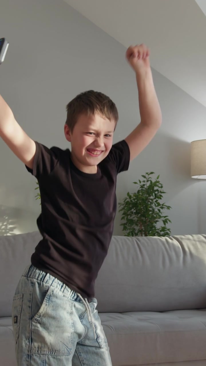 Young boy joyfully dances in living room holding smartphone expressing freedom and fun