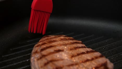 primer plano de una muñeca de mano de un bistec de ternera chamuscado en una sartén caliente recubierta con aceite de un cepillo rojo para una cena deliciosa