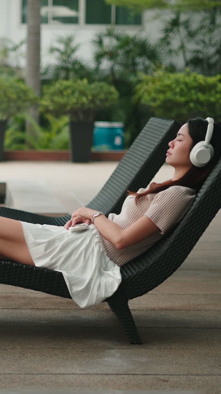 Giovane donna che si rilassa su una sedia a sdraio ascoltando musica con le cuffie
