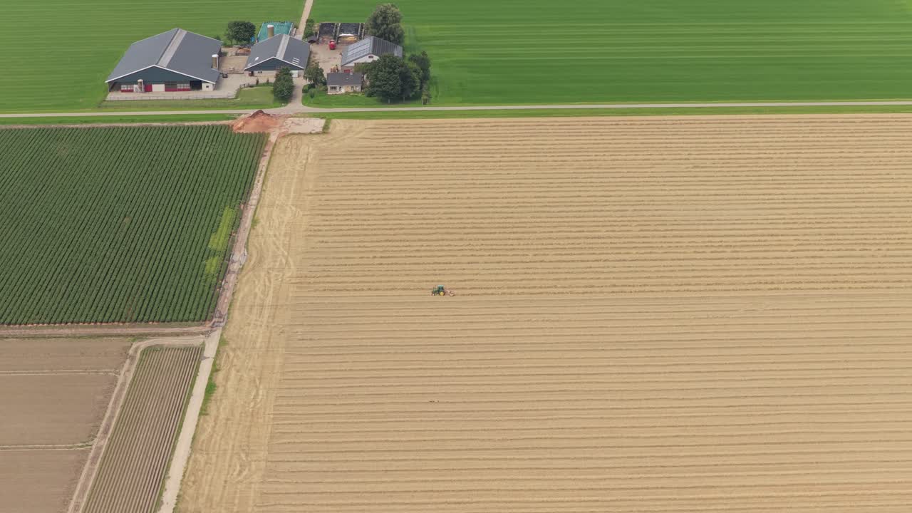 Veduta aerea con drone: trattore al lavoro in campagna con fienili sullo sfondo, Paesi Bassi