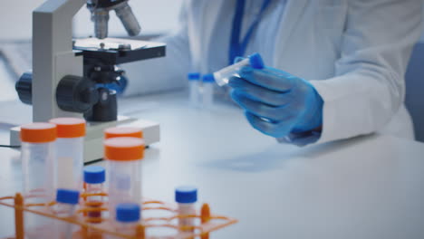 Close-Up-Of-Lab-Worker-Conducting-Research-Using-Microscope-Holding-Test-Tube-Labelled-Covid-19