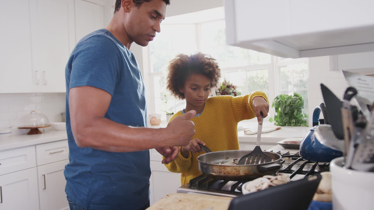 Gros plan sur une préadolescente afro-américaine et son père préparant un repas en suivant une recette sur une tablette numérique