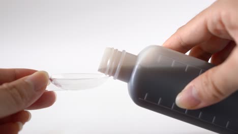 close up female hands pouring medicine syrup to measuring spoon from bottle for flu treatments