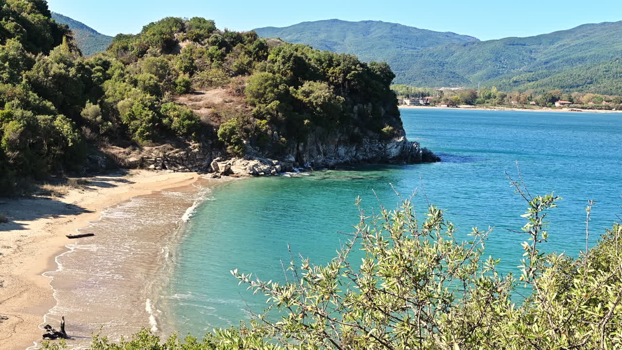 Aegean sea coast with beach, greenery around, rocks, bushes and trees, blue water, Greece