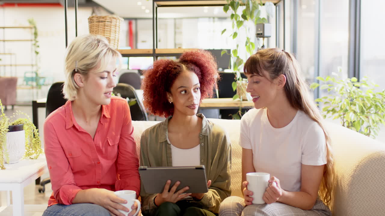 Discussing creative writing ideas, women holding tablet and coffee cups in office