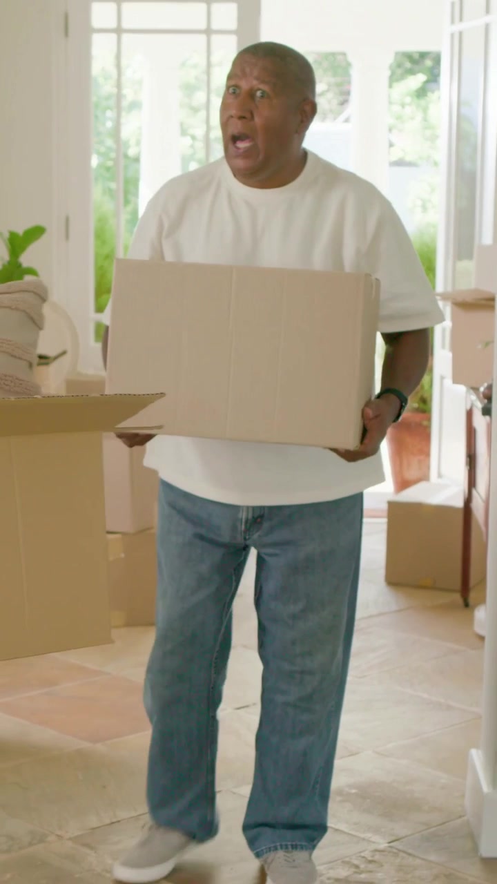 Vertical video: Entering foyer, door opening, senior man carrying box, placing boxes for move-in