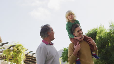 Vídeo-De-Un-Feliz-Padre-Caucásico-Cargando-A-Su-Hijo-Sobre-Los-Hombros-Y-Caminando-Con-Su-Abuelo-En-El-Jardín