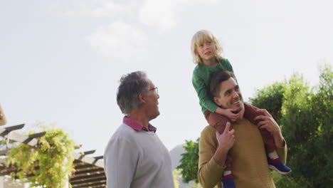 video of happy caucasian father carrying son on shoulders and walking with grandfather in garden