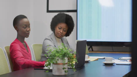 two african american businesswomen talking at office meeting, one holding paperwork