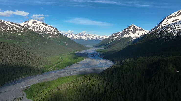 Letto di fiume in secca che attraversa una valle lussureggiante tra montagne parzialmente coperte di neve in Alaska, USA