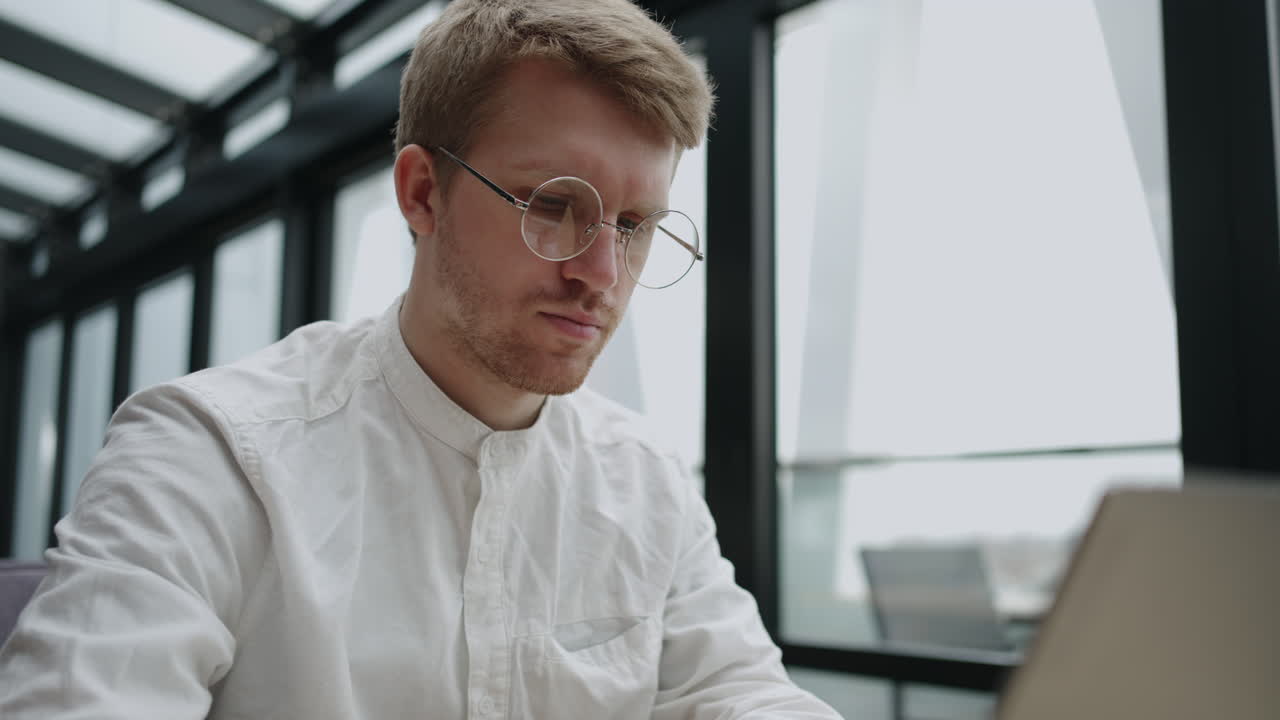 красивый молодой занятый мужчина, работающий в офисе, сидит за столом и работает на ноутбуке.